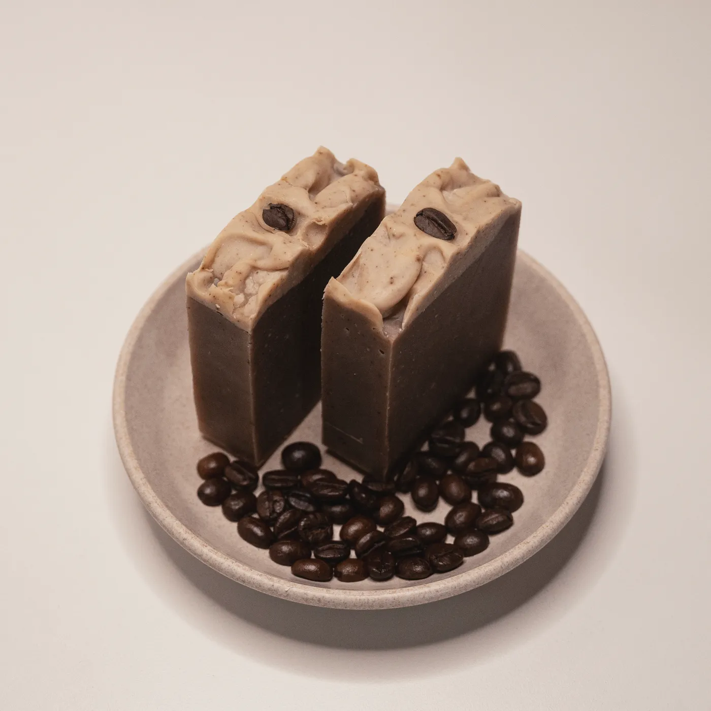 Two bars of Espresso coffee soap on a stone dish, scattered roasted coffee beans