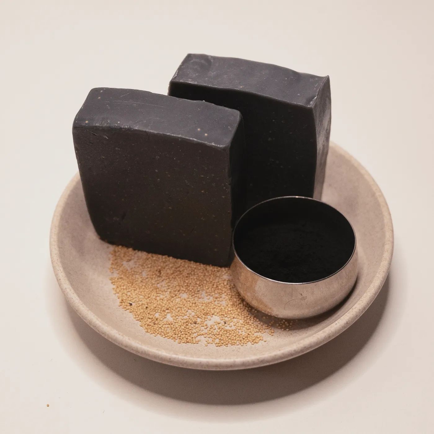 Two bars of Noir activated charcoal soap on a stone dish with charcoal powder