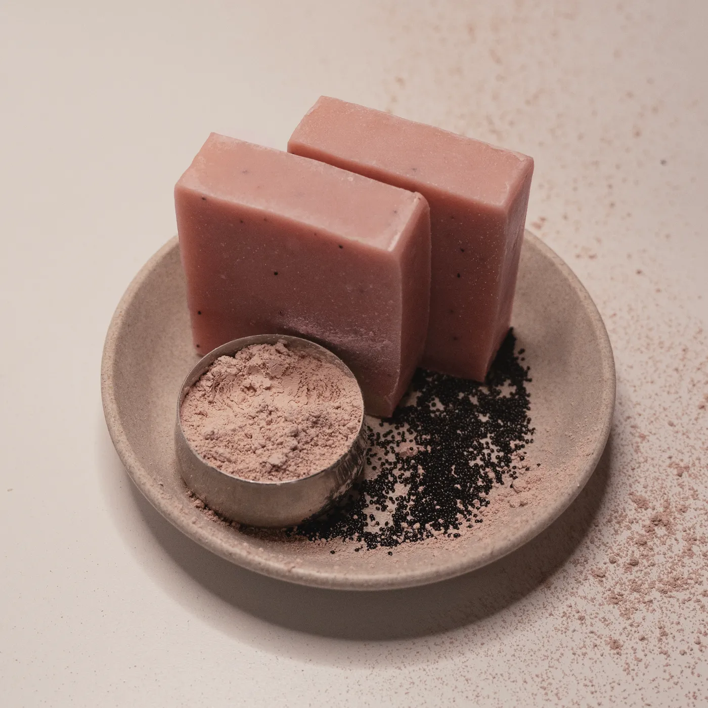 Two bars of Paris pink French clay soap on a stone dish beside a scoop of raw clay
