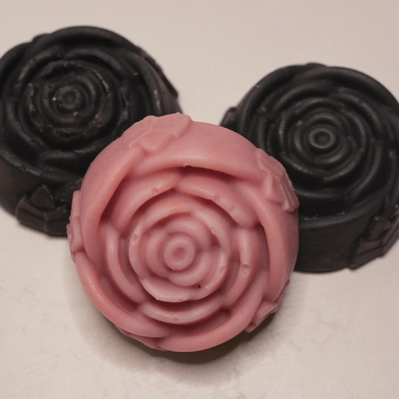 Three rose-moulded soaps, two charcoal and one pink clay
