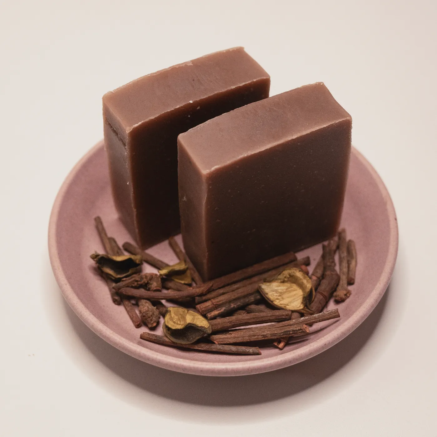 Two bars of Ruby Root manjistha soap on a pink dish with dried madder root