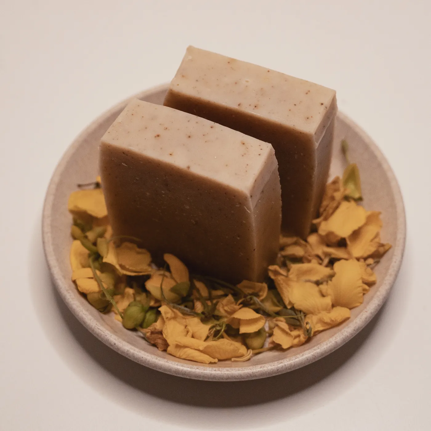 Two bars of తంగేడు tanner's cassia soap on a stone dish strewn with dried cassia flowers