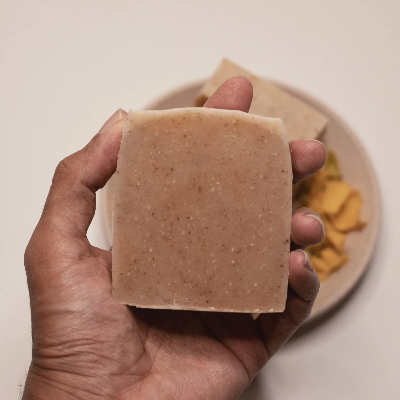 A bar of తంగేడు soap held in a hand, flecked with ground flower