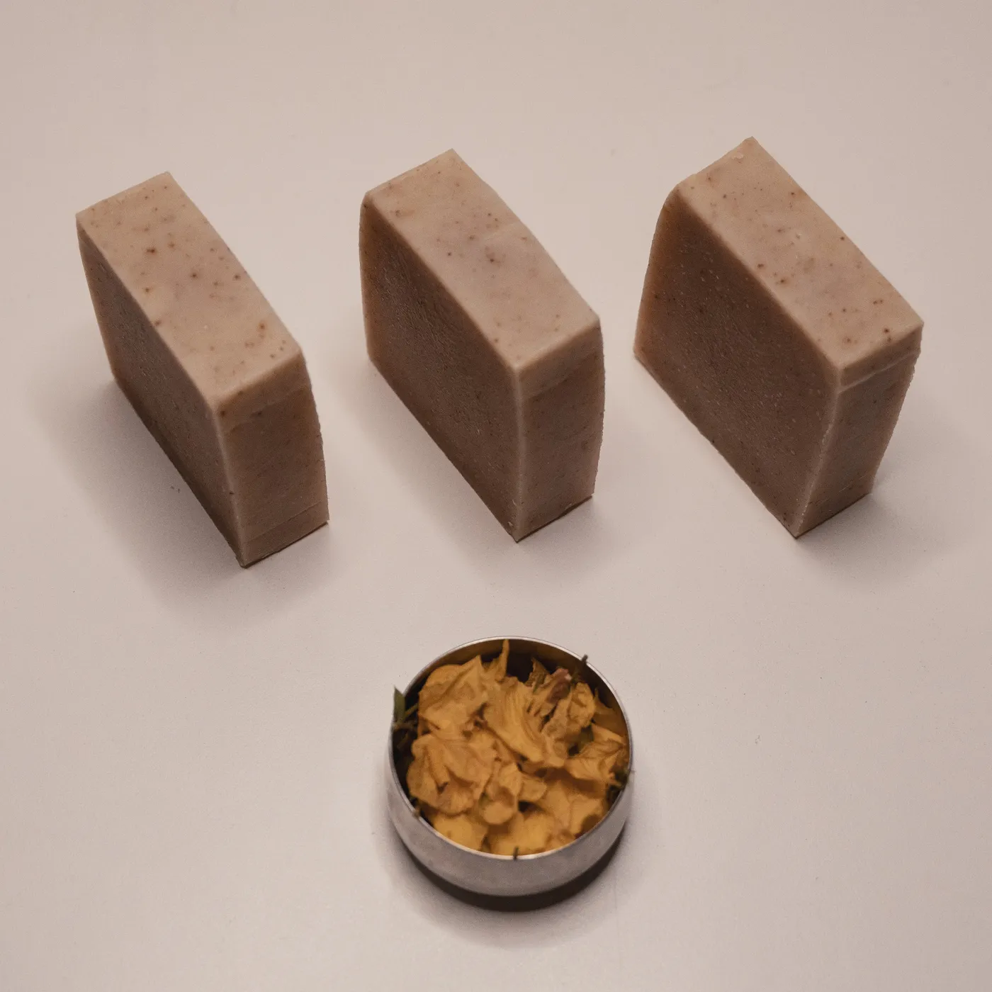 Three bars of తంగేడు soap in a row above a tin of dried cassia flowers